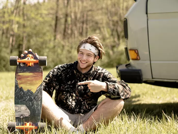 Vanlife picture on skateboard, in the hand of a young man